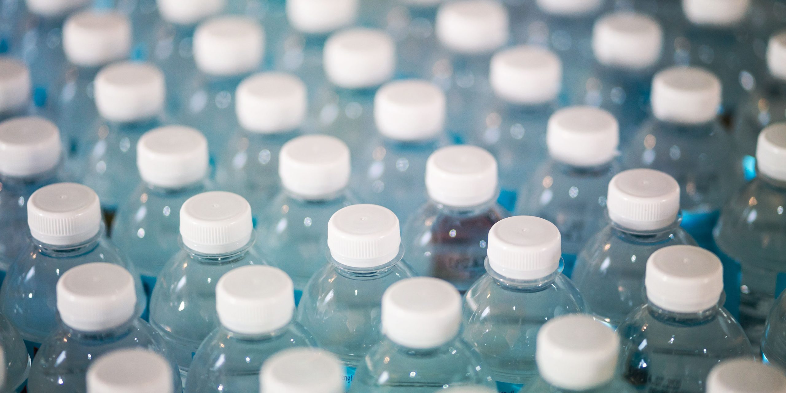 image shows a large grouping of clear plastic water bottles with lids being packaged. Source: Bottles-Photo-by-Jonathan-Chng-on-Unsplash