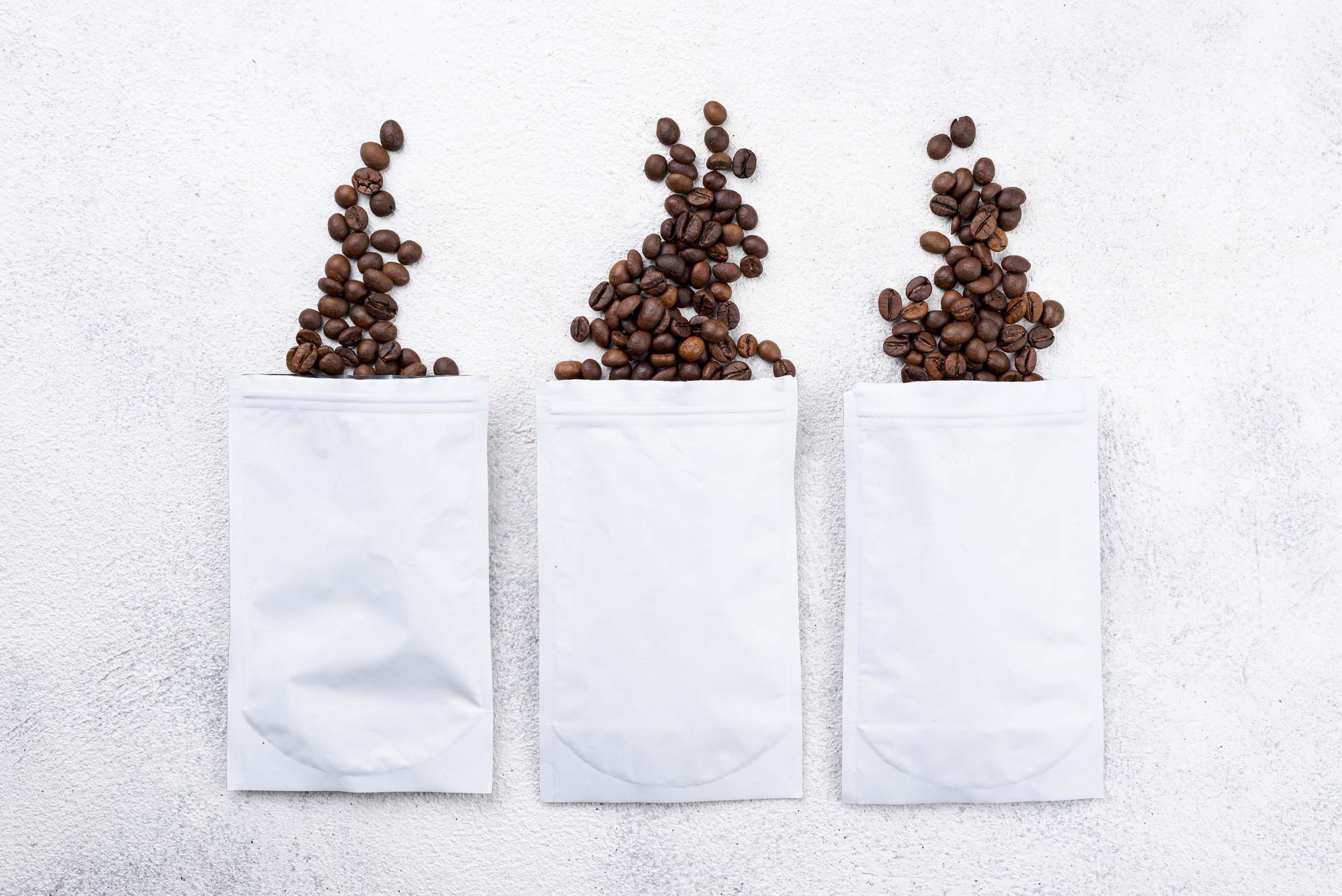 White lay flat pouches with coffee beans coming out from the top of the pouch