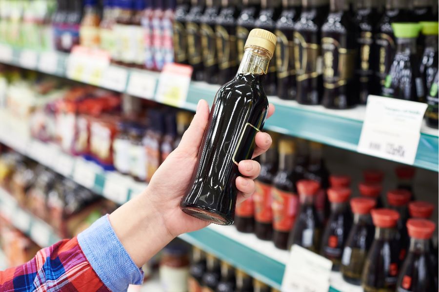 person in grocery aisle holding a bottle of brown sauce