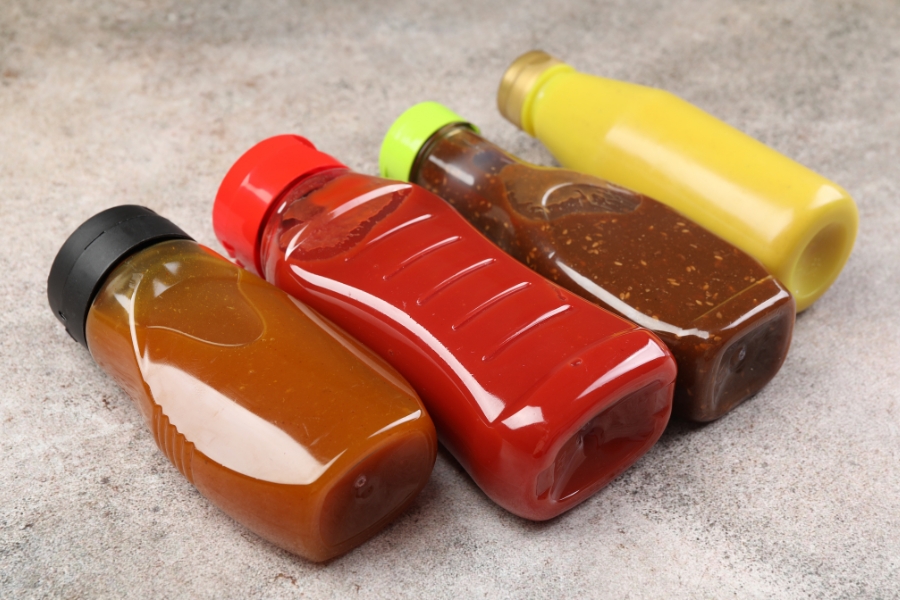 Barbeque sauce, ketchup, brown salad dressing, and yellow mustard bottles laying flat and side by side