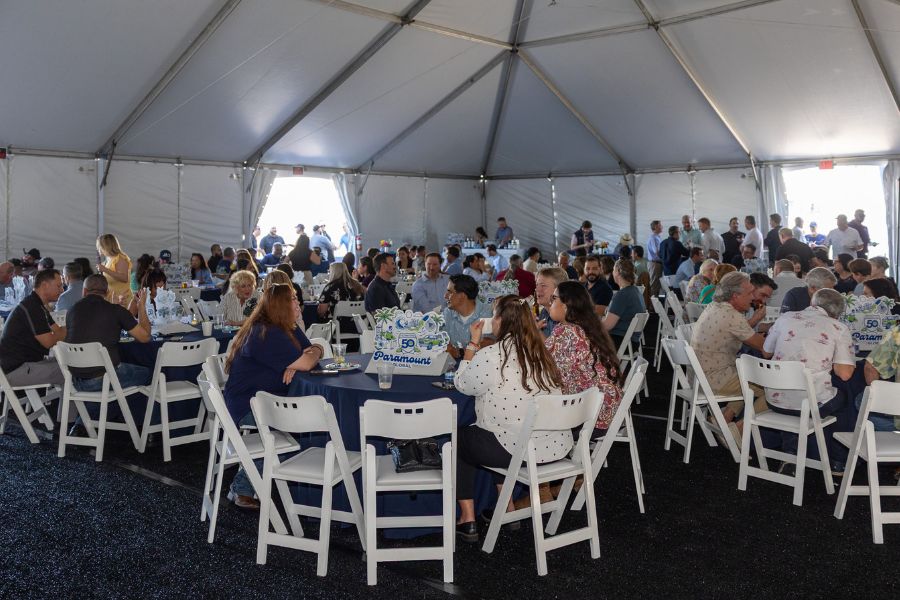Paramount Global 50th anniversary party. Attendees sitting at round tables inside white tent eating lunch and chatting.