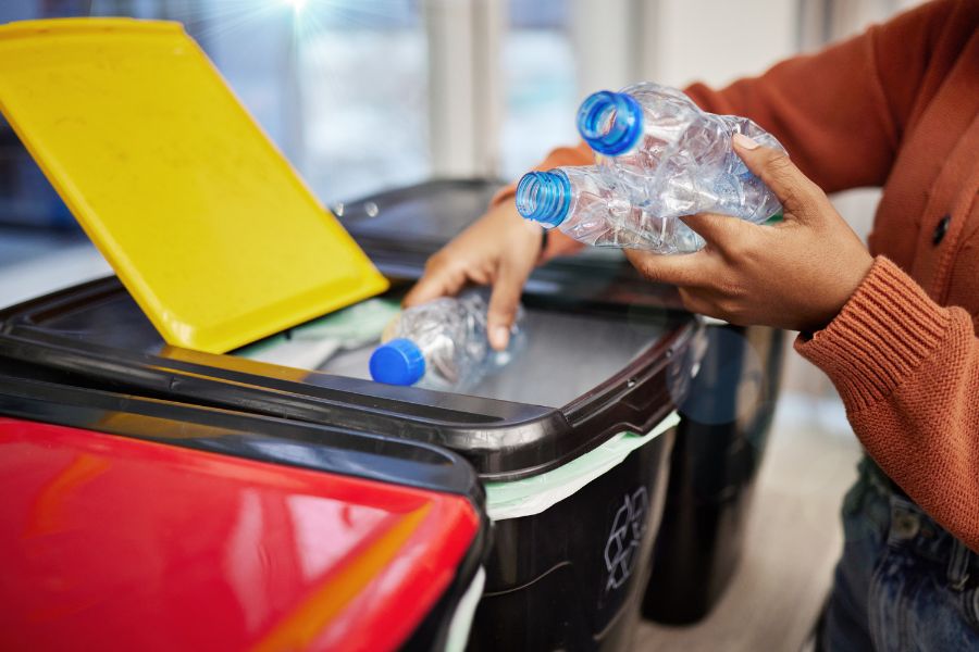 person sorting clear plastic water bottles into plastics recycling bin